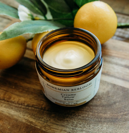 Jar of creamy tallow balm with lemons and leaves on a wooden surface