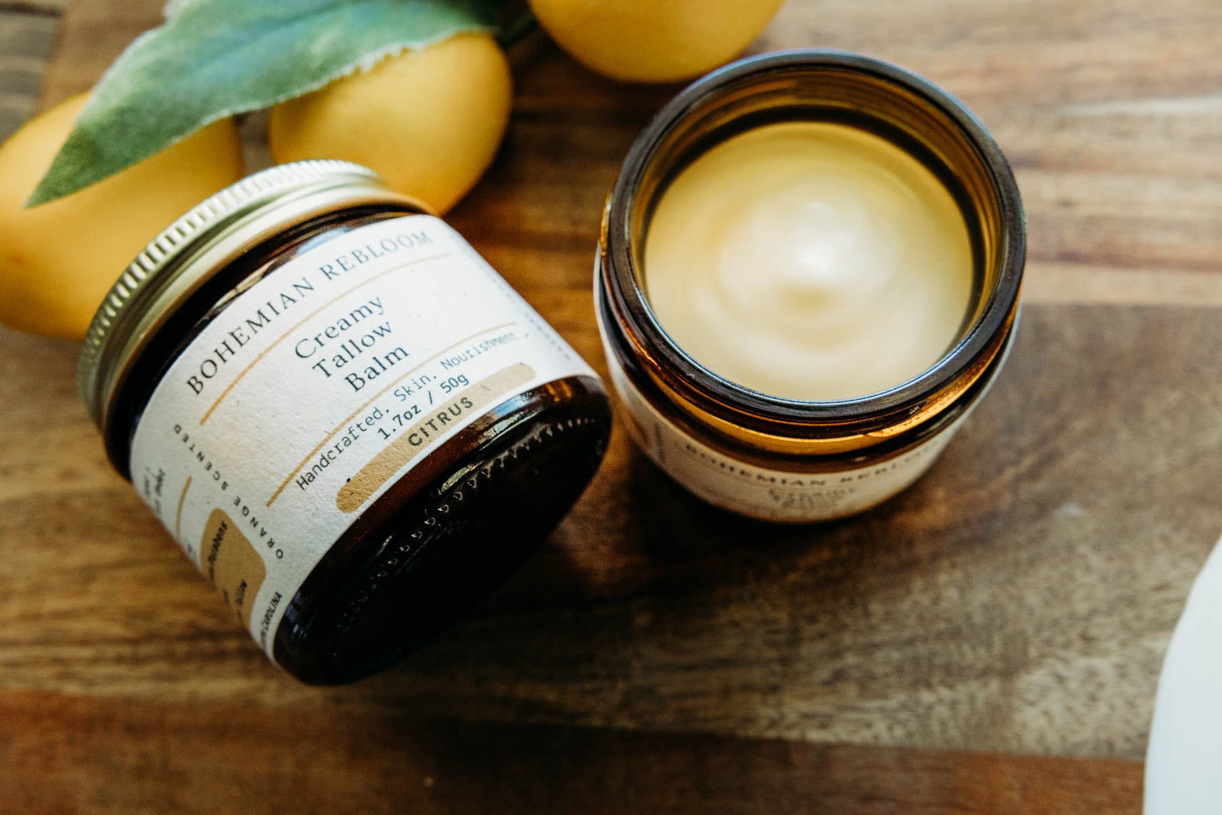 Two jars of Bohemian Rebloom creams citrus tallow balm on a wooden surface with lemons and leaves.
