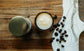 Small jar of Creamy Latte Tallow Balm next to a container of coffee beans on a wooden surface