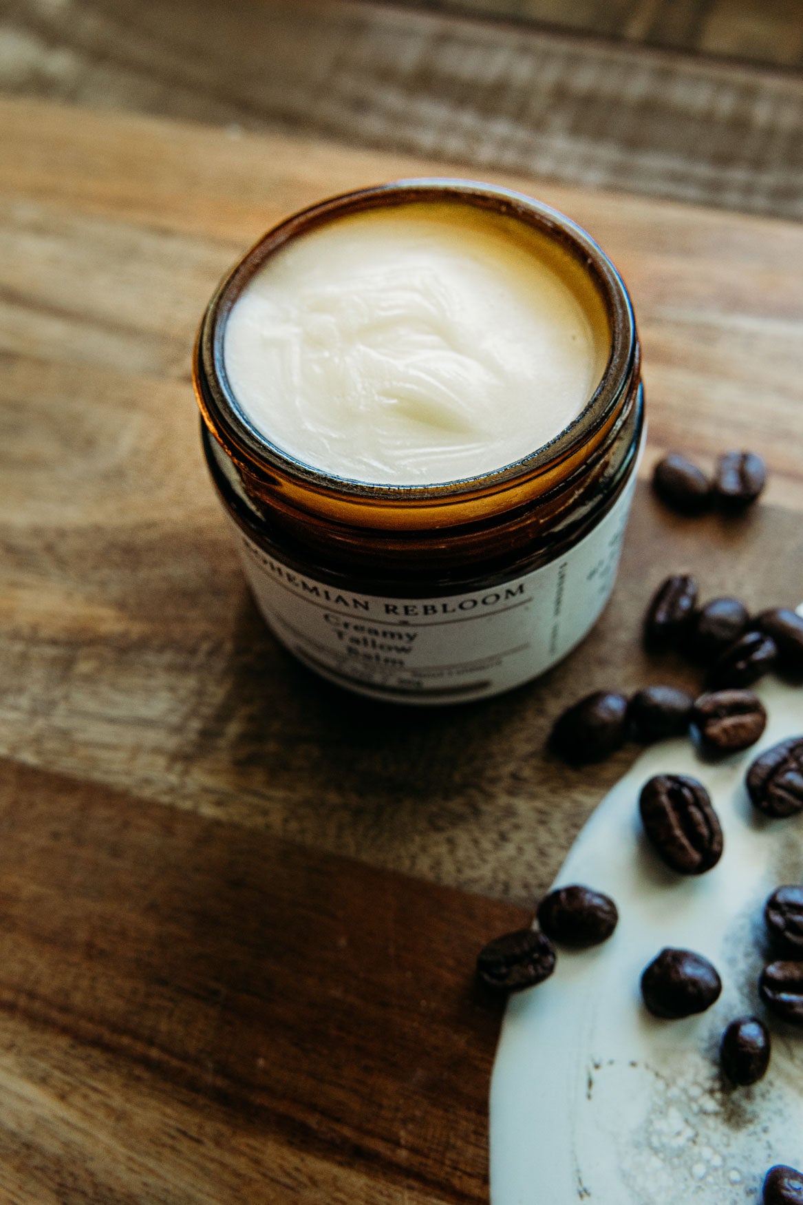Jar of creamy latte tallow balm on a wooden surface with coffee beans